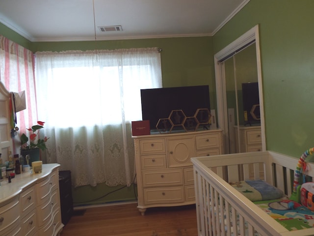 bedroom featuring ornamental molding, a crib, a closet, and dark hardwood / wood-style flooring