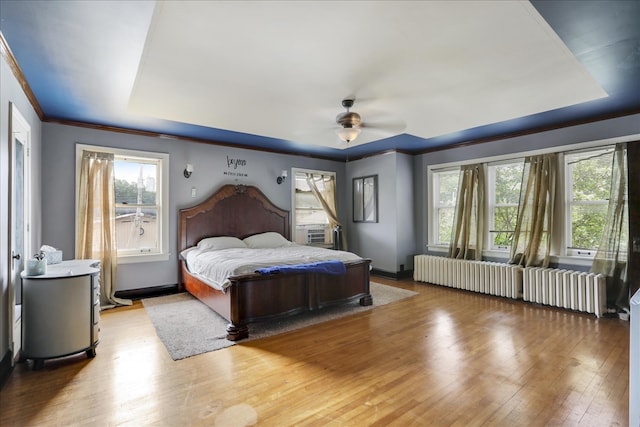 bedroom featuring light hardwood / wood-style floors, multiple windows, radiator heating unit, and ceiling fan