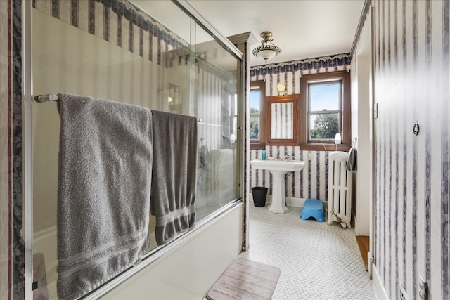 bathroom featuring enclosed tub / shower combo, sink, and radiator