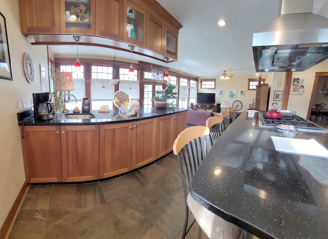 kitchen featuring hanging light fixtures, ceiling fan, dark tile floors, sink, and wall chimney exhaust hood