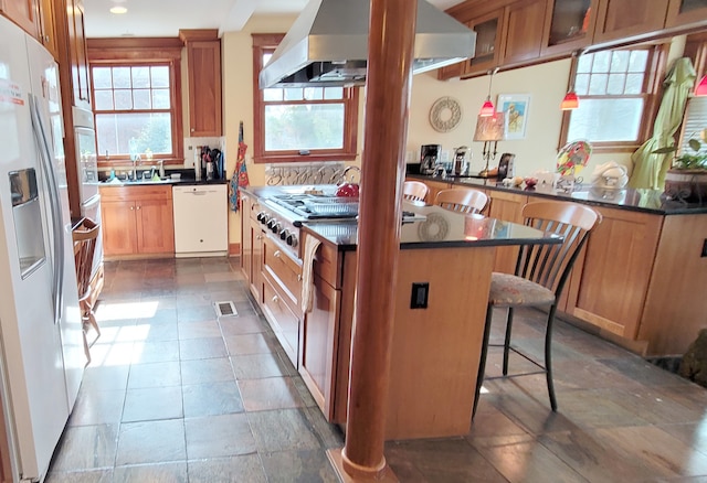 kitchen with tile floors, tasteful backsplash, white appliances, a kitchen breakfast bar, and wall chimney exhaust hood