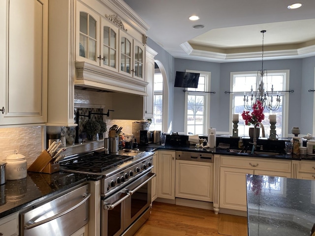 kitchen featuring sink, dishwasher, double oven range, hanging light fixtures, and a tray ceiling