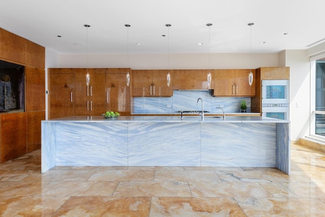 kitchen with tasteful backsplash, hanging light fixtures, multiple ovens, and sink