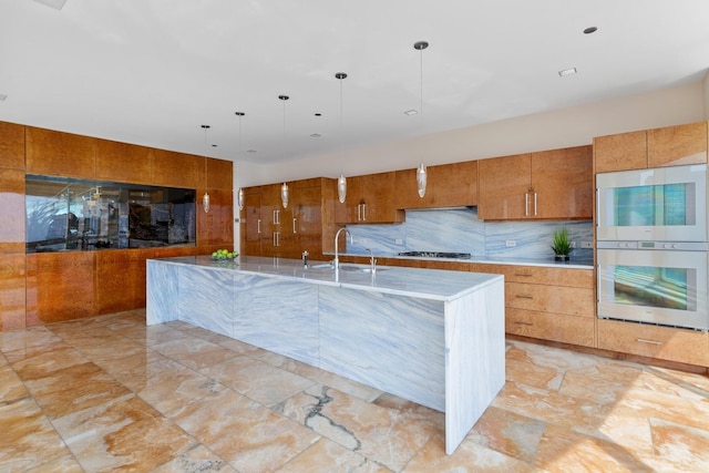 kitchen with appliances with stainless steel finishes, sink, decorative backsplash, hanging light fixtures, and a center island with sink