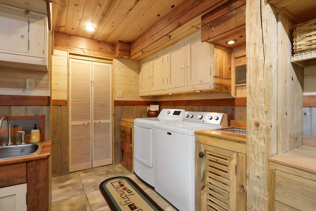 clothes washing area featuring wood walls, light tile floors, separate washer and dryer, cabinets, and sink