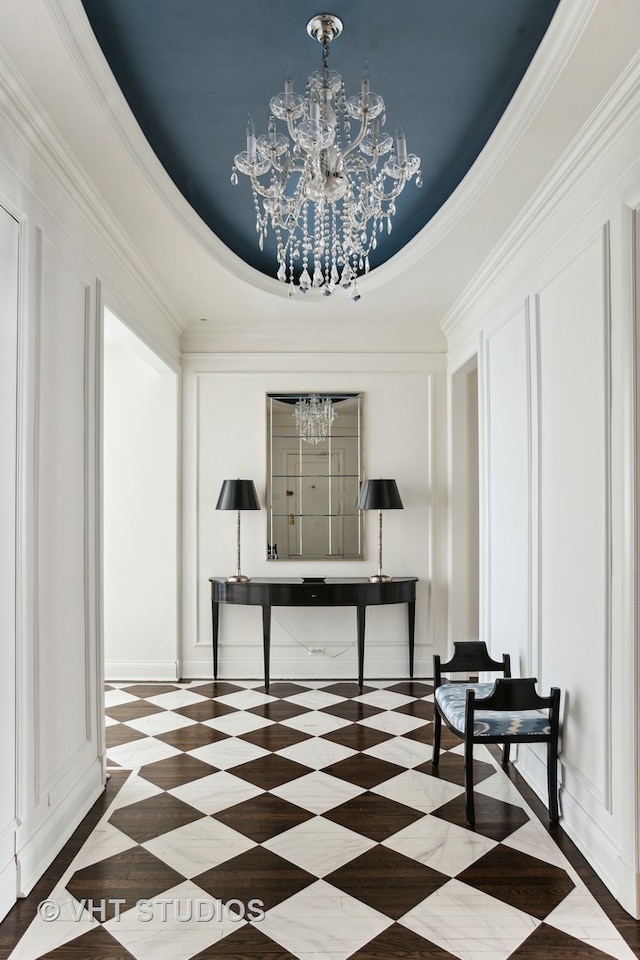 hall with tile flooring, a notable chandelier, ornamental molding, and a tray ceiling