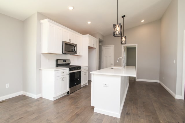 kitchen featuring decorative light fixtures, appliances with stainless steel finishes, an island with sink, white cabinets, and dark hardwood / wood-style flooring