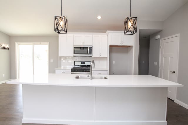 kitchen with decorative light fixtures, appliances with stainless steel finishes, an island with sink, white cabinets, and dark hardwood / wood-style flooring