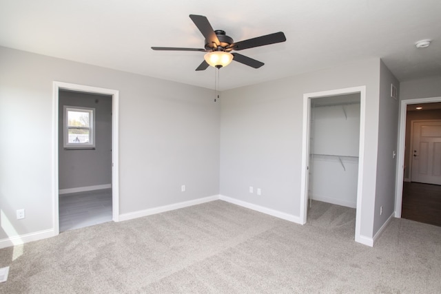 unfurnished bedroom with light carpet, a spacious closet, ensuite bath, and ceiling fan