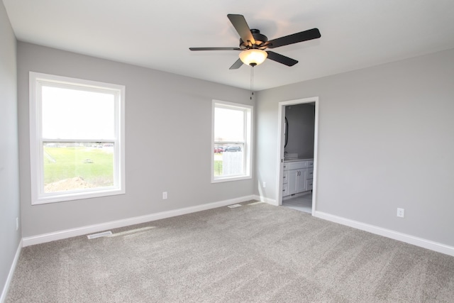 unfurnished bedroom with light carpet, multiple windows, ceiling fan, and ensuite bath