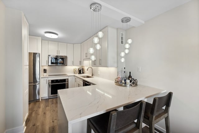 kitchen with kitchen peninsula, sink, a kitchen breakfast bar, stainless steel appliances, and decorative light fixtures