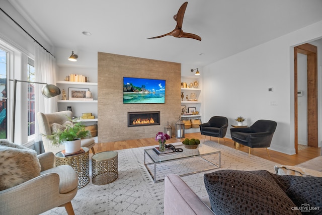 living room with a fireplace, light hardwood / wood-style flooring, built in shelves, and ceiling fan