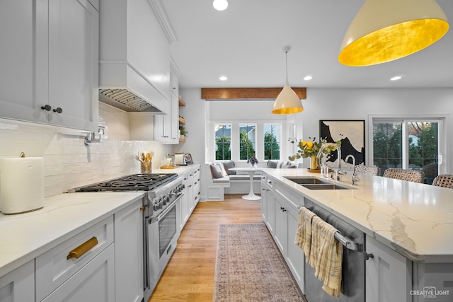 kitchen with custom range hood, light stone counters, stainless steel appliances, decorative light fixtures, and sink