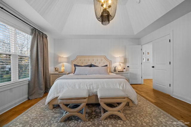 bedroom featuring a raised ceiling, an inviting chandelier, and light hardwood / wood-style floors