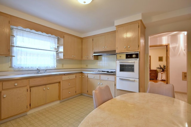 kitchen featuring white appliances, a sink, under cabinet range hood, backsplash, and light countertops