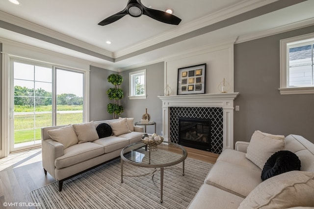 living room with ceiling fan, light wood-type flooring, a tile fireplace, and ornamental molding