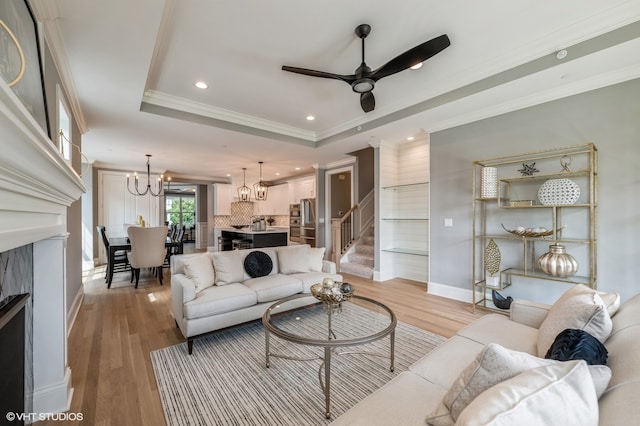 living room featuring light wood-type flooring, a raised ceiling, crown molding, and ceiling fan with notable chandelier