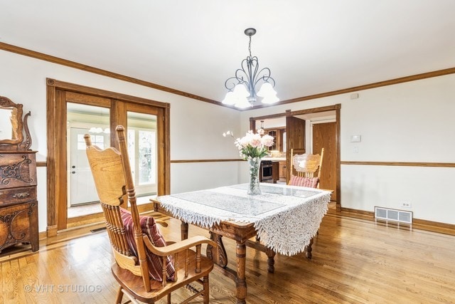 dining area featuring light hardwood / wood-style floors, ornamental molding, and a chandelier