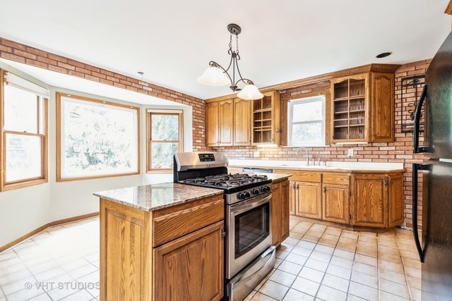 kitchen with stainless steel gas stove, black fridge, light tile floors, a center island, and hanging light fixtures