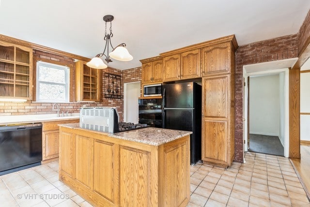 kitchen with pendant lighting, a kitchen island, brick wall, light tile flooring, and black appliances