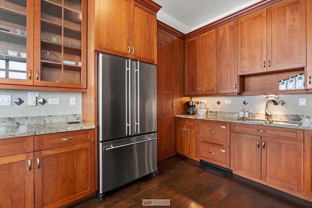 kitchen with light stone countertops, dark wood-type flooring, stainless steel fridge, backsplash, and sink