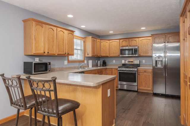 kitchen featuring kitchen peninsula, dark wood-type flooring, appliances with stainless steel finishes, sink, and a breakfast bar area