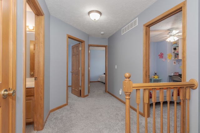 corridor with light carpet and a textured ceiling