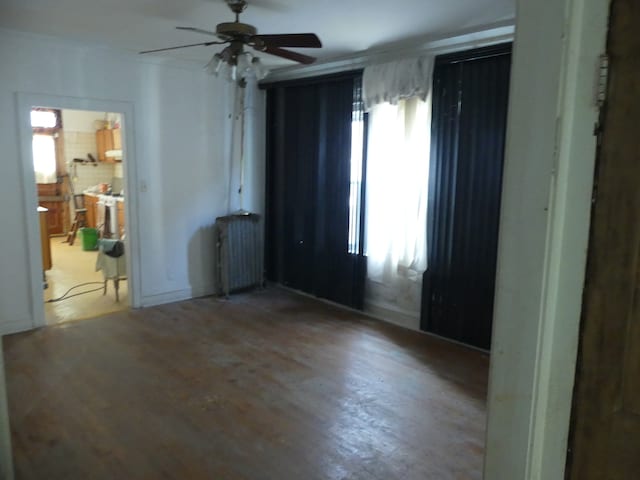 empty room with radiator heating unit, ceiling fan, wood-type flooring, and a wealth of natural light