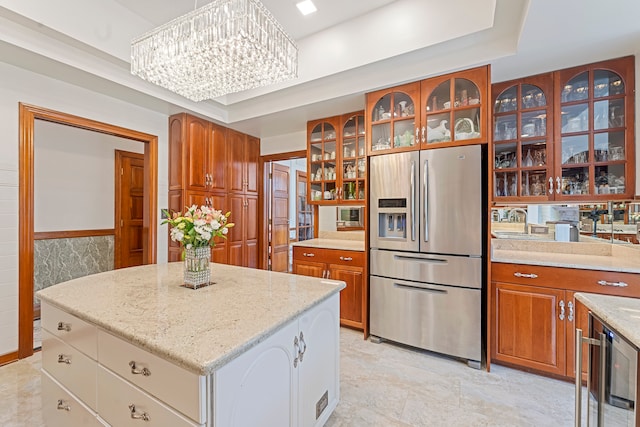 kitchen featuring stainless steel fridge with ice dispenser, a kitchen island, a raised ceiling, and a notable chandelier