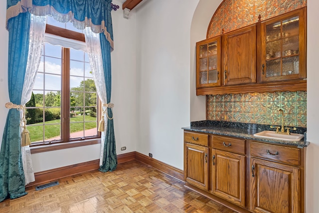 kitchen with light parquet floors, plenty of natural light, dark stone countertops, and sink