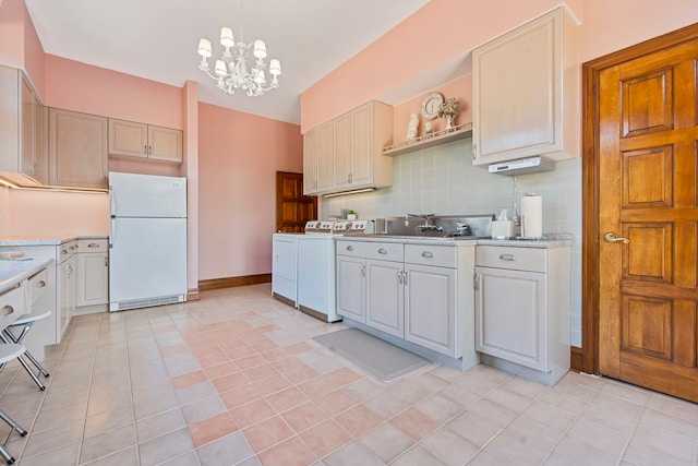 kitchen with decorative backsplash, washer and dryer, an inviting chandelier, white fridge, and hanging light fixtures