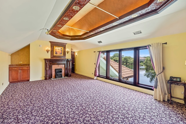 unfurnished living room with a raised ceiling, a tiled fireplace, carpet floors, and lofted ceiling