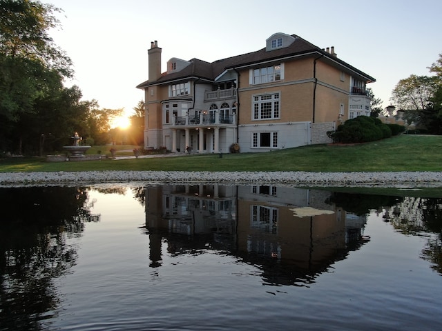 back house at dusk featuring a water view and a balcony