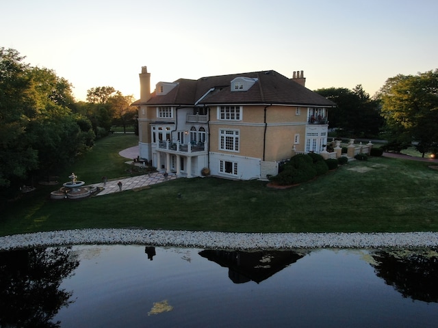 back house at dusk with a lawn and a water view