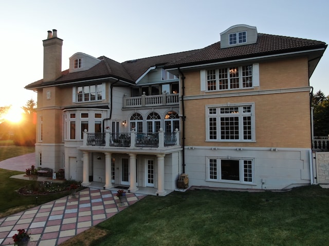 back house at dusk with a yard and a balcony