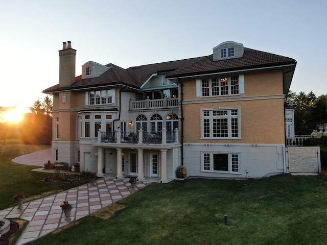 back house at dusk with a yard and a balcony