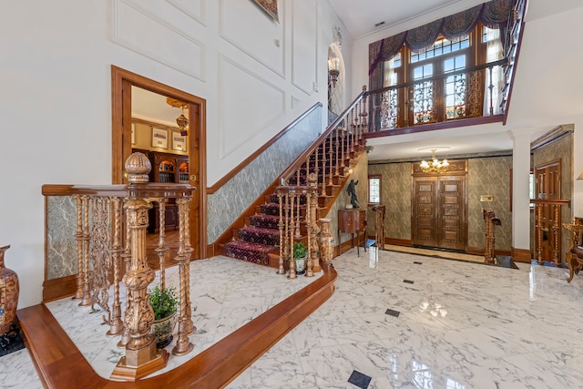 entrance foyer featuring ornate columns, ornamental molding, a high ceiling, and an inviting chandelier