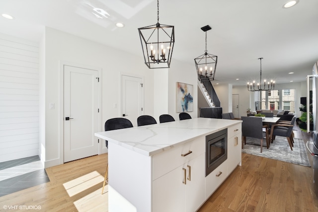 kitchen with a kitchen island, hanging light fixtures, stainless steel microwave, white cabinets, and light stone countertops