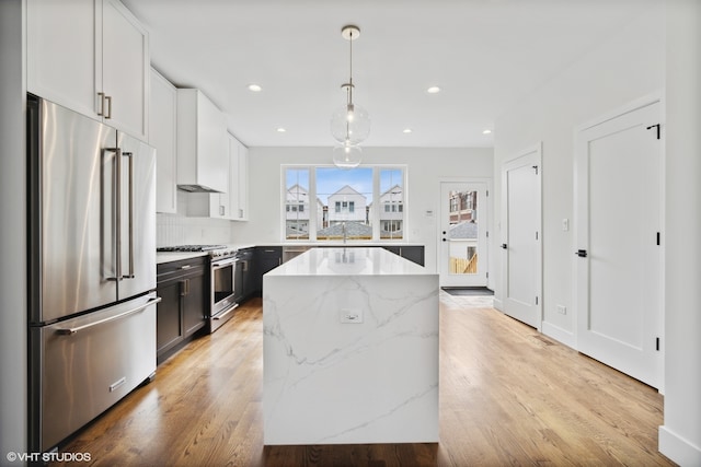 kitchen with white cabinetry, light wood-type flooring, a center island, high end appliances, and light stone countertops