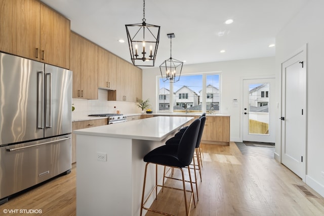 kitchen with appliances with stainless steel finishes, light hardwood / wood-style flooring, a center island, a chandelier, and tasteful backsplash