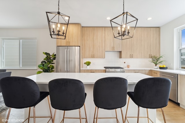 kitchen featuring light stone countertops, pendant lighting, light hardwood / wood-style flooring, and stainless steel appliances