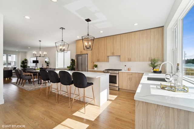 kitchen with appliances with stainless steel finishes, light brown cabinets, sink, light hardwood / wood-style flooring, and a kitchen island