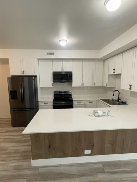 kitchen featuring fridge with ice dispenser, light wood-type flooring, sink, white cabinetry, and electric range