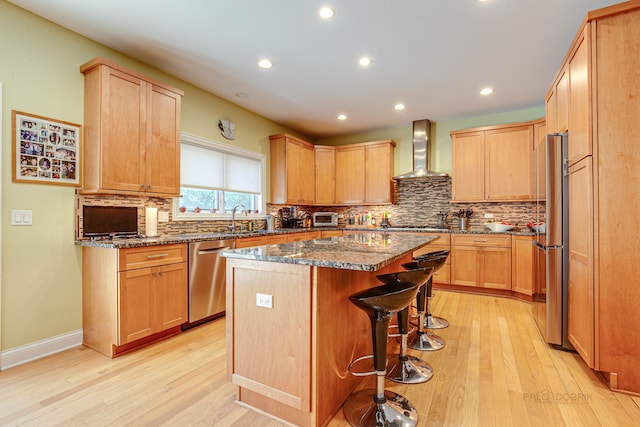 kitchen with wall chimney range hood, light hardwood / wood-style floors, appliances with stainless steel finishes, and a center island