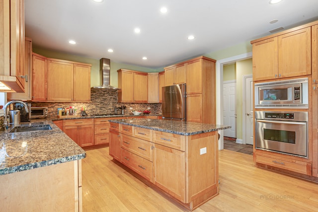 kitchen featuring dark stone countertops, stainless steel appliances, light hardwood / wood-style flooring, a center island, and wall chimney exhaust hood