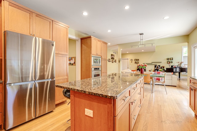 kitchen with light brown cabinetry, light stone counters, appliances with stainless steel finishes, light hardwood / wood-style floors, and a center island