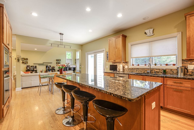 kitchen with sink, dark stone counters, a breakfast bar, light hardwood / wood-style floors, and a center island