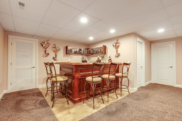 bar featuring a paneled ceiling and light tile flooring