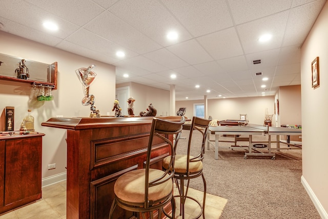 bar featuring a paneled ceiling and light tile flooring