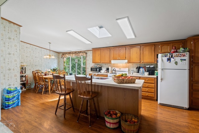 kitchen with an inviting chandelier, hanging light fixtures, white appliances, lofted ceiling with skylight, and light hardwood / wood-style flooring